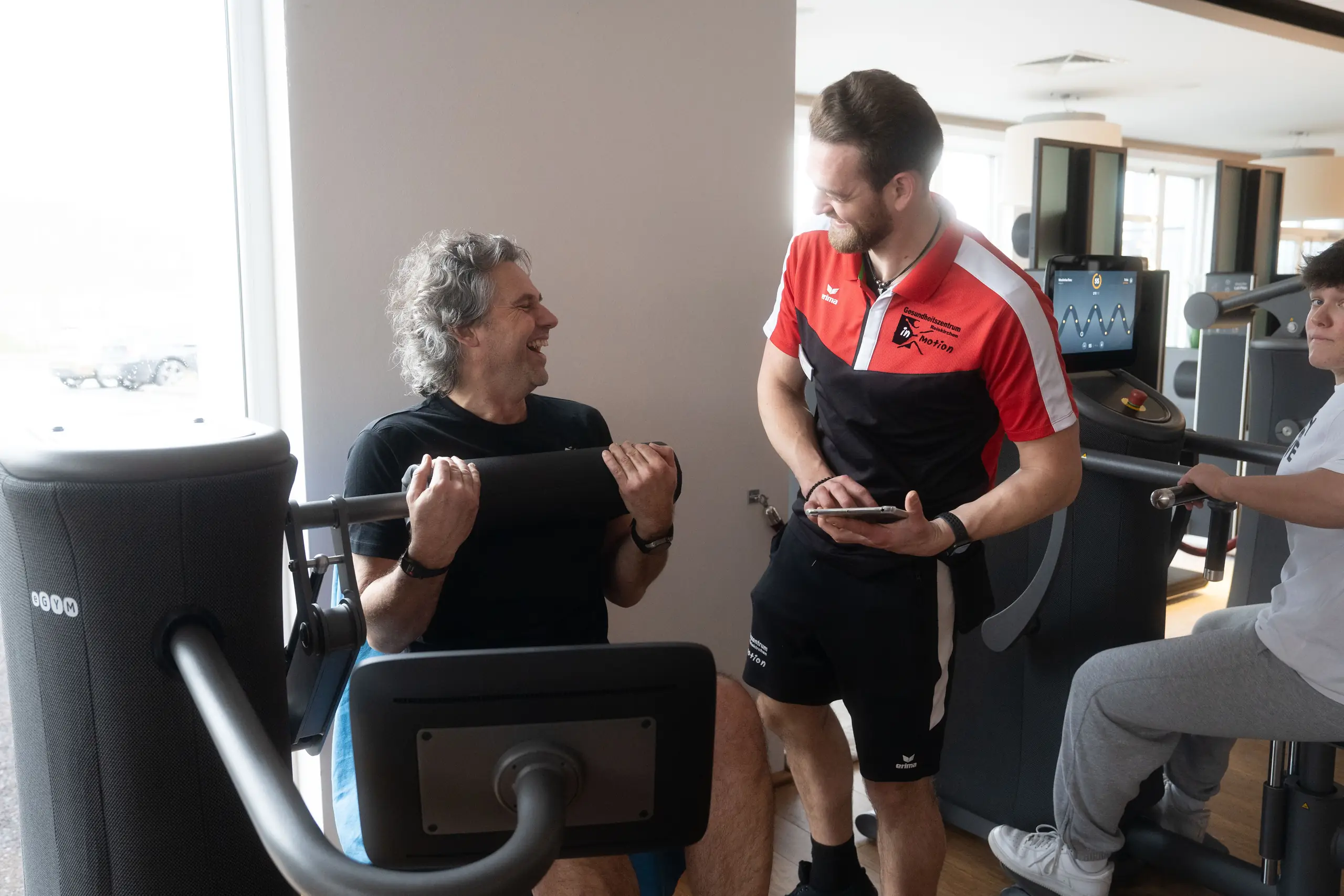 Mitglied lacht beim eGym-Training, Trainer daneben
